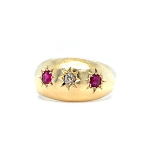 Op de afbeelding: Een gouden koepelring met drie horizontaal geplaatste stenen in een sterzetting. De middelste steen is een heldere, gefacetteerde diamant, geflankeerd door twee levendige, rondgeslepen robijnen. De ring heeft een gladde, gepolijste afwerking.