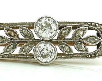 May include: A silver brooch featuring a delicate design of leaves and two round diamonds.