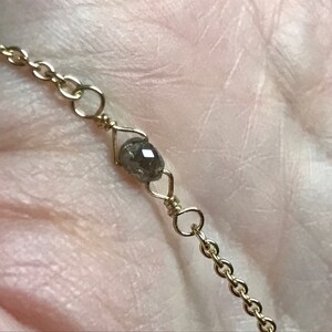 May include: A delicate gold chain necklace with a single, dark grey diamond bead.