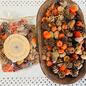 May include: A clear plastic bag of scented potpourri with a round tan label reading Scented Potpourri and sweetsaltybathshop.com, alongside an oval dark brown wooden bowl filled with a mix of pinecones, acorns, and small orange pumpkins.