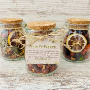 May include: Three glass jars with cork lids filled with dried fruit, spices, and citrus rinds. A label on the middle jar reads "Simmer Pot Potpourri" with instructions for use.