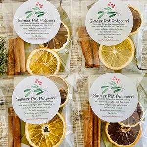 May include: Four clear plastic bags with white labels that say "Simmer Pot Potpourri" and instructions for use. Each bag contains dried orange slices, cinnamon sticks, and bay leaves. The bags are labeled with the names "Winter Wonderland", "Frankincense + Myrrh", "Winter Wonderland", and "Frankincense + Myrrh".