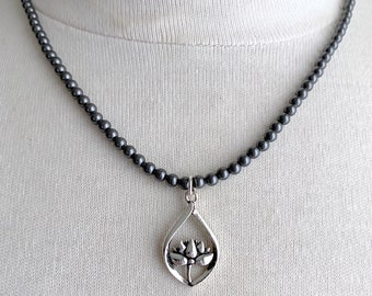 May include: A black beaded necklace with a silver lotus flower pendant.