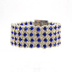 May include: A gold and blue beaded bracelet with a silver clasp. The bracelet is made with small, square beads in a geometric pattern.