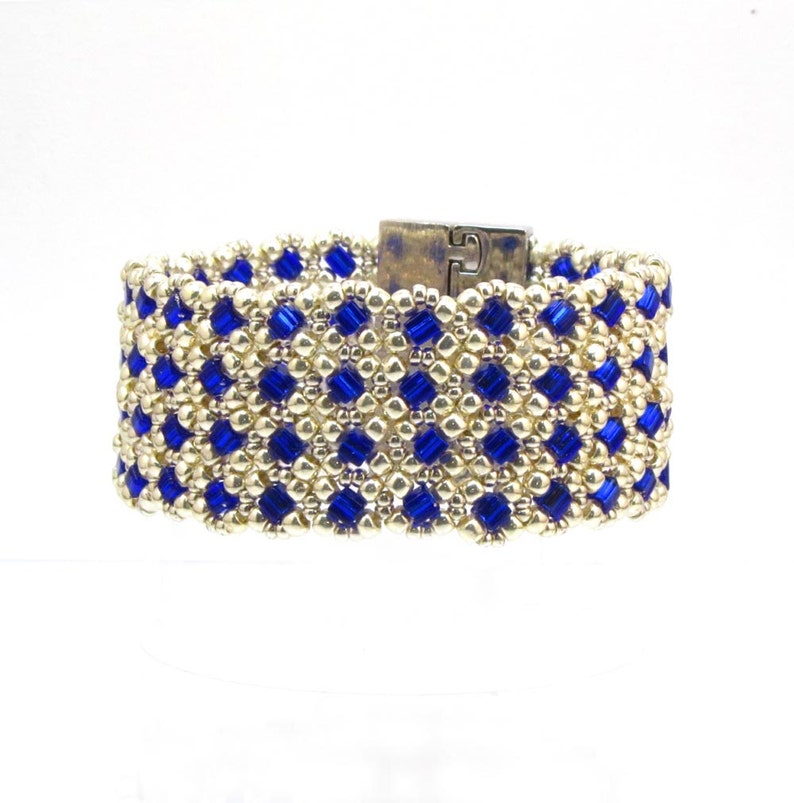 May include: A gold and blue beaded bracelet with a silver clasp. The bracelet is made with small, square beads in a geometric pattern.