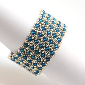 May include: A blue and silver beaded bracelet with a geometric pattern. The bracelet is made with small, round beads and is designed to fit comfortably on the wrist.