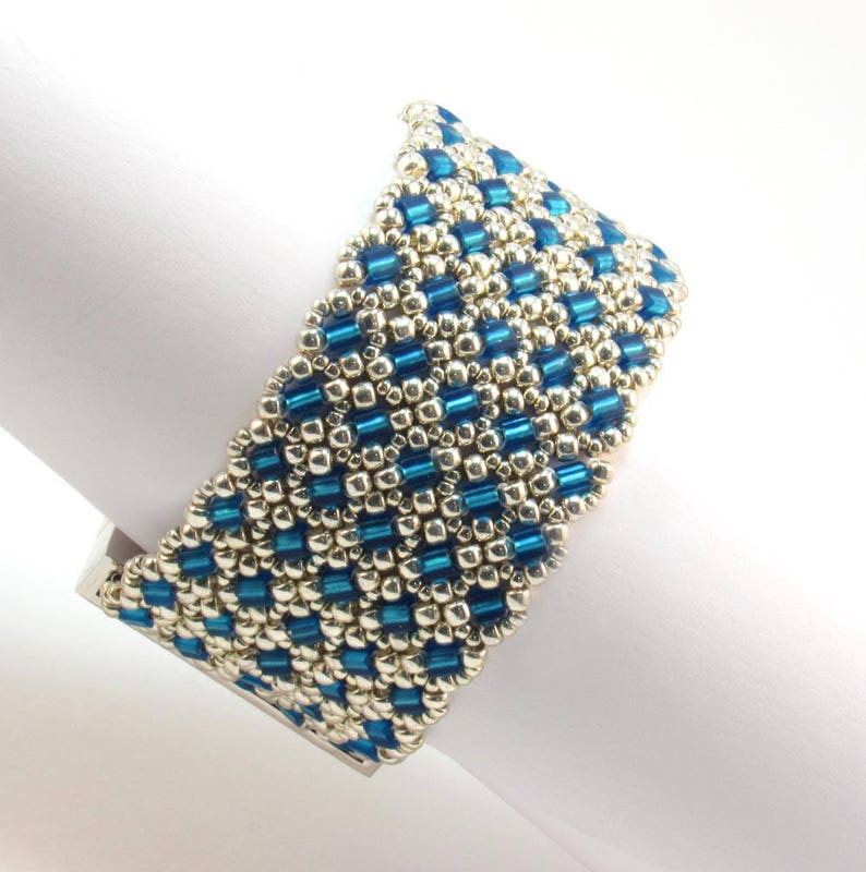 May include: A blue and silver beaded bracelet with a geometric pattern. The bracelet is made with small, round beads and is designed to fit comfortably on the wrist.
