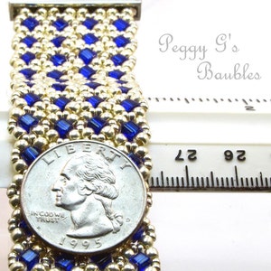 May include: A gold and blue beaded bracelet with a silver quarter for scale. The bracelet is approximately 2 inches wide and is made with small, square beads. The text "Peggy G's Baubles" is visible in the image.