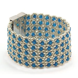 May include: A silver and blue beaded bracelet with a silver clasp. The bracelet is made with small, square beads in a geometric pattern.