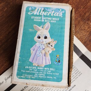 May include: A vintage Alberta's Student Casting Mold box. The box features a teal background with a cartoon bunny holding a doll. The text reads "#A-313 GIRL BUNNY WITH DOLL" and "3 3/4" high - 9.5 cm high".