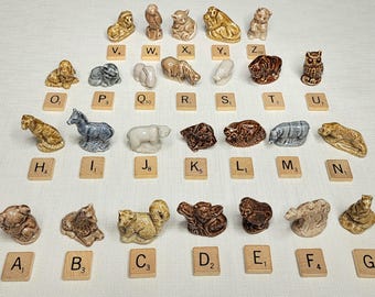 May include: A collection of small animal figurines, including a lion, owl, and bear, arranged with Scrabble tiles. The figurines are in various colors, such as brown, gray, and tan. The tiles have letters and numbers.