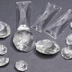 May include: A collection of clear, faceted crystal pendants and decorative elements. The assortment includes rectangular, trapezoid, and various geometric shapes, all designed to catch and reflect light. Ideal for jewelry making or decorative projects.