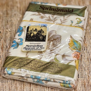 May include: A packaged set of Springmaid Metropolitan Museum of Art Adaptations pillowcases. The pillowcases feature a floral pattern in shades of blue, yellow, and brown on a cream background. The package includes two standard pillowcases, each measuring 20 x 26 inches (51 x 66 cm).