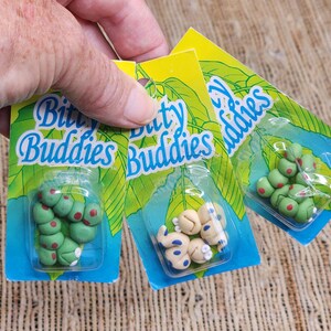 May include: Three Bitty Buddies blister packs featuring small clay-like figurines. One pack contains green caterpillars with red spots, another holds beige creatures with blue spots, and the third displays green round shapes with red spots.