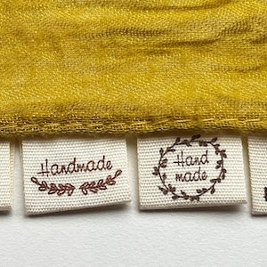 May include: Six different handmade fabric labels with various designs. The labels are white with brown text and designs. The labels read "handmade with heart", "handmade", "handmade", "hand made", "handmade", and "handmade".