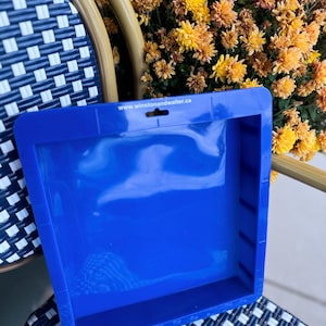 Könnte beinhalten: Eine leuchtend blaue Kunststoffschale mit rechteckiger Form und einem kleinen Loch oben. Die Schale steht auf einem Stuhl mit einem schwarz-weißen Webmuster. Die Website-Adresse www.winstonandwalter.ca ist auf der Schale aufgedruckt.