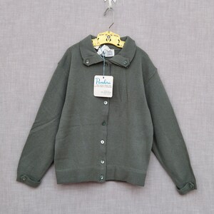 May include: A green cardigan with a button-up front and a collared neckline. The cardigan has a tag that reads "Pandora The Vogue Shop 100% Acrylic".