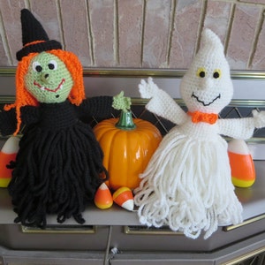 Puede incluir: Decoraciones de Halloween de ganchillo con una bruja de pelo naranja y vestido negro, y un fantasma blanco con pajarita naranja. Una calabaza de cerámica y caramelos de maíz completan la exhibición festiva.