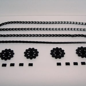 May include: Black plastic chain links and gears for a model building kit. The chain is in three pieces, and there are four gears and five small black plastic pieces.