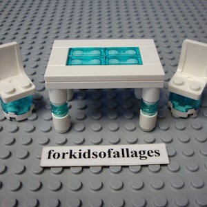 May include: A white Lego table with four teal-colored inserts and two matching chairs. The table has four white legs with teal accents. The chairs have a white seat and teal-colored bases. The text "forkidsofallages" is on a white rectangle.