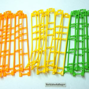 May include: Three sets of track pieces for a toy race car set. The pieces are made of plastic and are in the colors orange, yellow, and green.