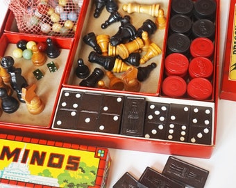 May include: A red box filled with various board games, including dominoes, checkers, chess, and a game called "Minos". The box also contains red and black game pieces.