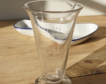 May include: A clear glass measuring cup with a wide base and a spout. The cup has markings in ounces and pints. The cup is sitting on a wooden surface.