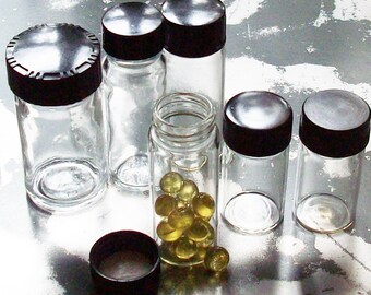 May include: Six glass jars with black lids, some filled with small yellow pills. The jars are on a silver surface.