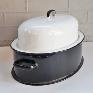 May include: Oval black and white enamelware casserole dish with a lid. The dish has a black base with a white rim and a white lid with a black handle. The casserole dish is designed for cooking and serving.