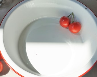 May include: A white enamelware bowl with a red rim, featuring two red tomatoes on a green vine. The bowl is empty and has a white interior.