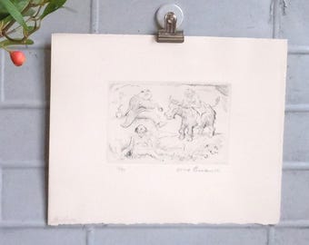 May include: A rectangular off-white paper print featuring a black ink etching of three figures and a donkey in a landscape. The print is held by a silver metal clip. The etching depicts a seated figure, a reclining figure, and a figure riding a donkey.