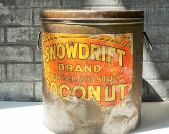 May include: Vintage metal can with a rusty exterior and a faded label that reads "Snowdrift Brand Sweetened Fancy Shred Coconut".