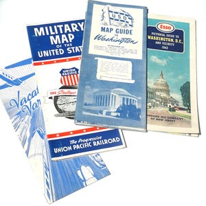 May include: A collection of vintage travel guides and maps, featuring titles like "Military Map of the United States" and "Map Guide to Washington." The guides have blue and white color schemes, with illustrations of landmarks and transportation.