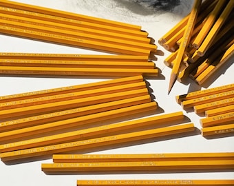 May include: A close-up of a pile of yellow wooden pencils with the text "KOH-I-NOOR E&G HARDTMUTH" printed on the side of the pencils.