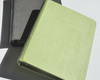 May include: Two notebooks, one black and one green, are stacked on top of each other. The notebooks are closed and have a textured fabric cover.