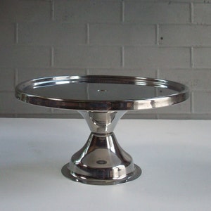 May include: A silver cake stand with a round, mirrored top and a flared base. The stand is made of metal and has a smooth, polished finish.