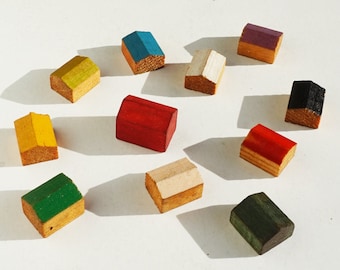 May include: Ten wooden toy houses in various colours, including red, blue, green, yellow, white, black, and purple. The houses are all different sizes and shapes, and they are arranged in a circle on a white surface.