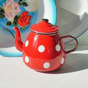 May include: Red enamel teapot with white polka dots. The teapot has a black handle and spout.