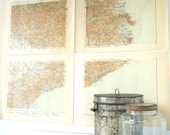 May include: Four vintage maps with tan and brown tones are displayed on a white wall. A metal container and a clear glass jar with a lid sit in front of the maps. The maps appear to be of a coastal region.