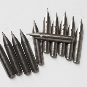 May include: A collection of 10 vintage metal nibs for fountain pens. The nibs are silver in color and have various inscriptions, including "Old Pen", "Manifold Pen", and "J.S. Manifold Book & Co's."