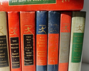 May include: A collection of ten vintage paperback books with red, blue, and white spines. The books are part of the Modern Library series and feature titles such as "The Maltese Falcon", "All the King's Men", and "The Prince of the Discouragers".