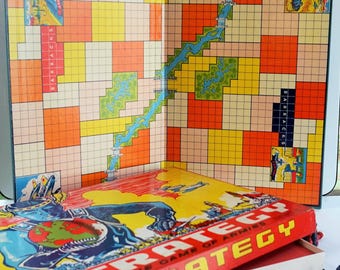 May include: Vintage board game called "Strategy, The Game of Armies". The game board is open and shows a map with a river and squares. The box is red with a black and blue illustration of a soldier holding a globe. The game pieces are red and black.
