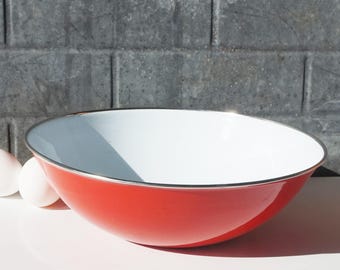 May include: A large, red enamel bowl with a white interior and a silver rim. The bowl is sitting on a white surface.