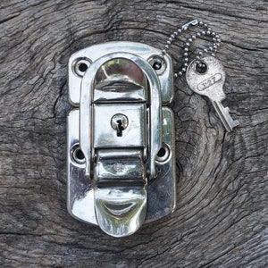 May include: A silver metal latch with a keyhole and a silver key attached to a chain. The latch is on a wooden surface.
