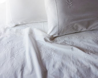 May include: White bedding with embroidered floral designs. The bedding is made of a soft, white fabric and features delicate floral patterns.