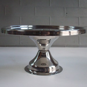 May include: A silver cake stand with a round top and a wide base. The stand is made of metal and has a shiny finish.