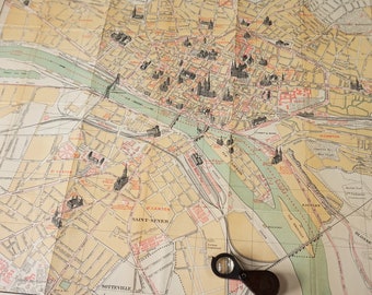 May include: A vintage map of Rouen, France, with a magnifying glass on top. The map is printed on a cream-colored paper and shows the city's streets, buildings, and landmarks. The map is titled "Plan Monumental de Rouen".
