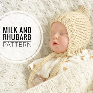 May include: A baby wearing a beige knitted hat with earflaps. The hat is called "Milk and Rhubarb Pattern".
