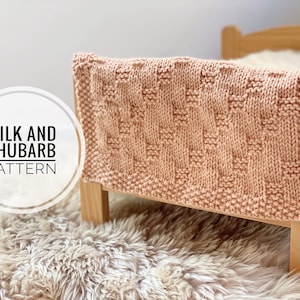 May include: A pink knitted baby blanket with a textured pattern. The blanket is draped over a wooden crib with a white mattress. The text "Milk and Rhubarb Pattern" is visible in the image.