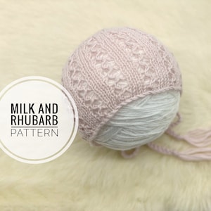 May include: A pink knitted baby hat with a lacy pattern and ties. The hat is on a white ball of yarn and a white fluffy surface. The text "Milk and Rhubarb Pattern" is in a white circle.